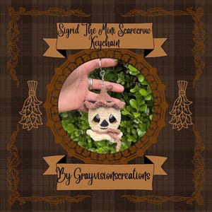 May include: A crochet scarecrow keyring featuring a cream-coloured head, a brown textured hat, and a matching brown scarf. The character has large black eyes and a small stitched mouth. The text Sigrid The Mini Scarecrow Keychain By Grayvisionscreations is displayed on the frame.
