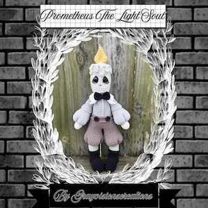Puede incluir: Muñeca de ganchillo con forma de vela y llama amarilla. Viste camisa gris, pantalones cortos marrones y zapatos negros. El texto "Prometheus The Light Soul" y "By Grayvisionscreations" se muestran en la imagen.