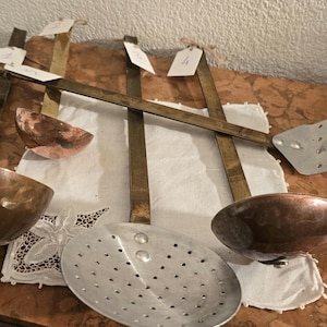 Op de afbeelding: Een set van vier vintage keukengerei, waaronder twee koperen lepels, een schuimspaan en een platte spatel. De keukengerei hebben houten handvatten en zijn gerangschikt op een wit tafelkleed.