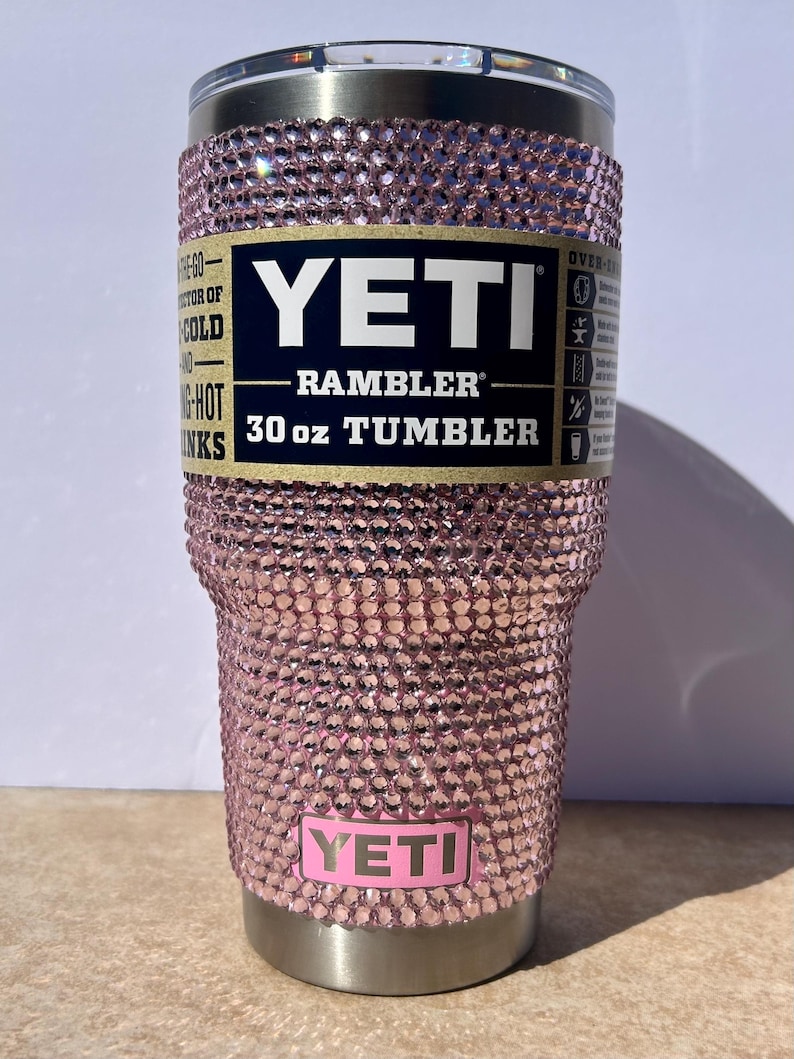 May include: A pink Yeti Rambler 30 oz tumbler with a pink rhinestone design. The tumbler has a stainless steel lid and base.