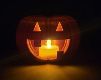 Può includere: Una zucca arancione intagliata con ritagli triangolari per gli occhi e una bocca sorridente. Una candela gialla accesa è all'interno, che proietta un bagliore caldo. La decorazione di Halloween è su uno sfondo scuro.