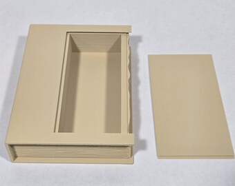 May include: A beige rectangular storage box with a hollow interior and a separate flat lid. The exterior features a textured side panel resembling the pages of a book, while the main body has a smooth, solid finish and a clean, open rectangular cavity.