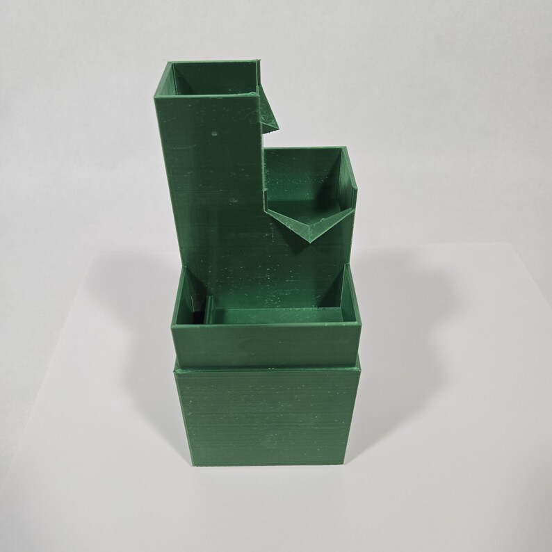 May include: A dark green, multi-tiered, 3D-printed plastic structure featuring a tall rectangular tower section on the left, a mid-height basin in the centre, and a wide base section at the bottom, designed with open compartments and spillways.