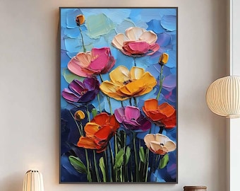 May include: A framed floral painting featuring vibrant, textured flowers in shades of pink, orange, yellow, and purple against a blue background. The artwork is a close-up of the flowers, with visible brushstrokes, and is displayed in a modern living room setting.
