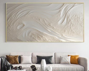 May include: Abstract white and cream textured wall art with a gold frame. The art is hanging above a white sofa with pillows.