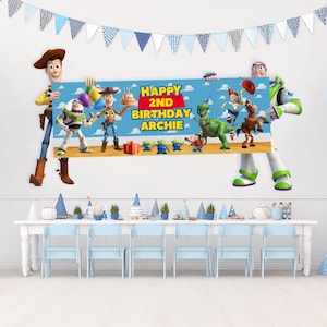 Könnte beinhalten: Eine Geburtstagsparty-Szene mit Toy Story-Charakteren. Ein Banner mit der Aufschrift "Happy 2nd Birthday Archie". Der Tisch ist mit blauen Stühlen, Partyhüten und Dekorationen gedeckt. Ein blau-weißes Banner hängt darüber.
