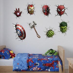 Op de afbeelding: Kinderslaapkamer met een bed met een blauw superhelden-thema dekbedovertrek en kussen. De muur is versierd met 3D muurstickers van Marvel-personages, waaronder Iron Man, Captain America en Spider-Man.