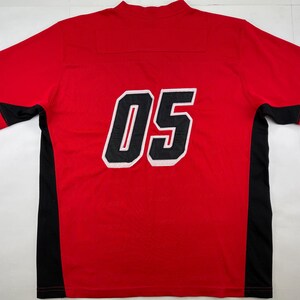 May include: Red athletic jersey with black side panels and sleeves. The number "05" is displayed on the back in white with a black outline. The jersey has a crew neck.