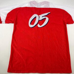 May include: Red and white jersey with a white number "05" on the back. The jersey has red and white stripes on the sleeves.