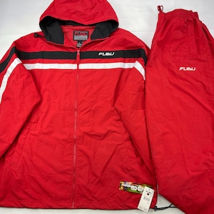 May include: Red Fubu tracksuit set. The jacket has a hood, a black and white stripe design, and the Fubu logo. The trousers are solid red with the Fubu logo. The jacket has a zip closure and a drawstring at the bottom.