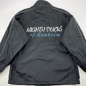 Op de afbeelding: Zwarte windbreaker-jas met witte piping en de tekst "Mighty Ducks of Anaheim" op de rug.