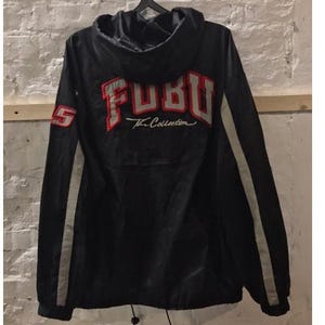 May include: Black hooded jacket with white and red FUBU The Collection logo on the back. The jacket has white stripes on the sleeves.
