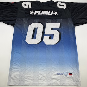 Può includere: Maglia nera e blu con il numero 05 in bianco. La maglia presenta la scritta "FUBU" sul petto e il numero 5 sulla spalla sinistra. La maglia ha un design sfumato.