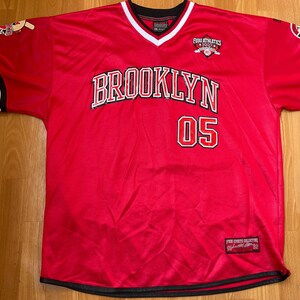 May include: Red mesh jersey with "BROOKLYN 05" in white and red lettering. Features black and white striped sleeves, a V-neck with white trim, and a small logo on the chest. The jersey has a black hem and sleeve cuffs.