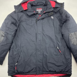 Peut inclure: Veste d'hiver noire avec doublure et bordure de capuche rouges. La veste a une fermeture éclair, plusieurs poches et un petit logo sur la poitrine. Les manches ont des patchs renforcés. Conçue pour le froid.