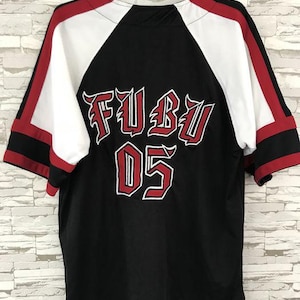 May include: Black baseball jersey with white and red detailing. The back displays the text "FUBU" in red with a white outline, and the number "05" beneath. The jersey has short sleeves and is suspended from a black hanger.