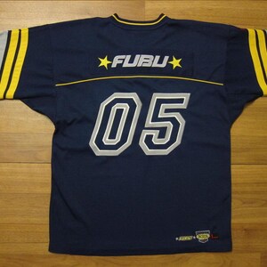 May include: A navy blue jersey featuring the text FUBU with yellow stars on the upper back. The number 05 is printed in large white and grey numerals on the centre back. The sleeves are grey with yellow stripes and the number 05 on each shoulder.