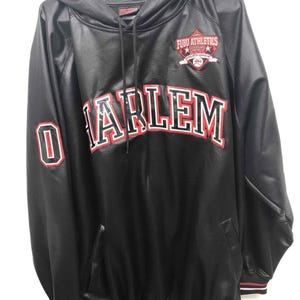 May include: A black hooded sweatshirt with a smooth finish, featuring the word HARLEM in large red and white letters across the chest. A FUBU ATHLETICS 1992 patch is on the upper left chest, and the number 0 is on the right sleeve with red trim.