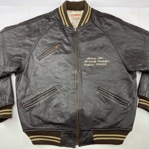 Pu&ograve; includere: Giacca bomber in pelle marrone con chiusura a zip, due tasche frontali e polsini e orlo a coste. La giacca presenta la scritta "Avirex Ltd. Normandy Campaign England 1942-43" ricamata sul petto.