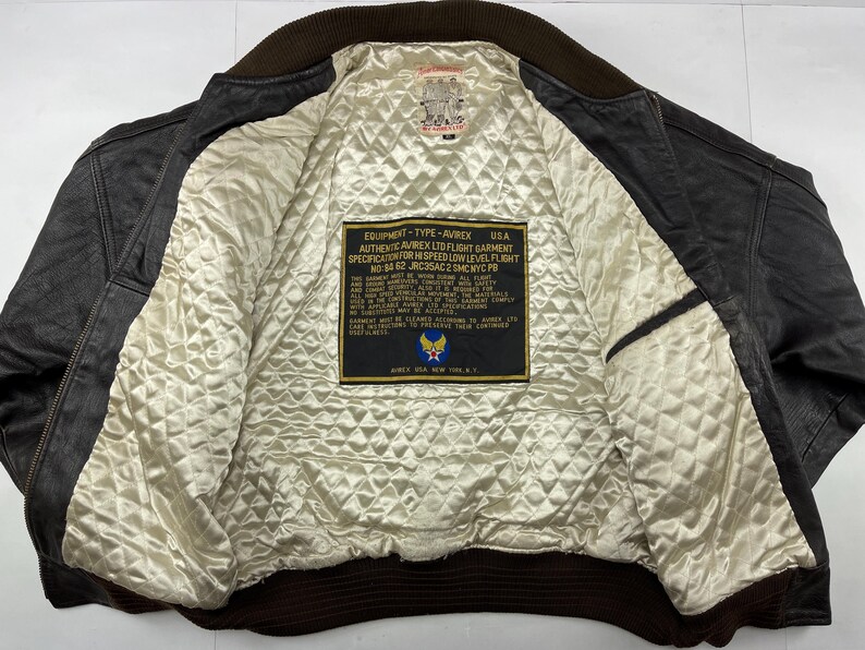 Pu&ograve; includere: Giacca bomber vintage in pelle marrone con fodera trapuntata color crema. La giacca presenta colletto e polsini a coste marroni. All'interno, un'etichetta mostra il testo "AVIREX USA" e "AUTHENTIC AVIREX LTD FLIGHT GARMENT".