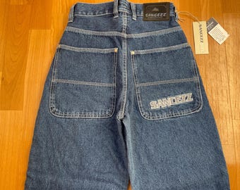 May include: Back view of blue denim jeans with white stitching. The jeans have two back pockets and a logo on the right pocket. A leather patch with a logo is on the waistband. A tag with the brand name is attached.