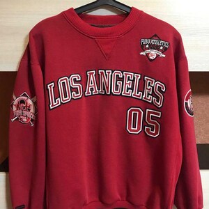 May include: Red crew neck sweatshirt with "LOS ANGELES" in white and black lettering, and the number "05". Features "FUBU ATHLETICS" logo on the chest and sleeves. Black trim at the bottom and cuffs.