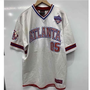 May include: White baseball jersey with red and blue trim. The jersey has "Atlanta" and "05" on the front, and a logo that says "Fubu Athletic League 1992" on the chest.