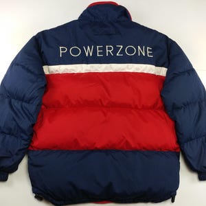 May include: A navy blue, red, and white puffer jacket with the word "POWERZONE" embroidered across the back. The jacket features a red midsection, white stripe, and navy blue sleeves and collar.