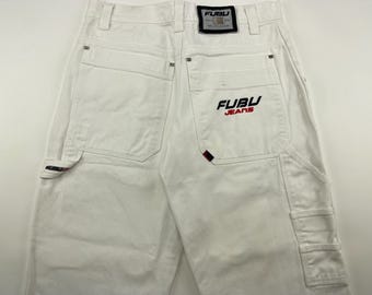 May include: White denim pants with multiple pockets, including a carpenter-style pocket. The back features the "FUBU JEANS" logo in red and black. A small red accent is visible on the back pocket. The pants have a classic, casual style.