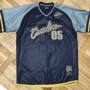 May include: A navy blue and light blue jersey with the word "Carolina" in gold script and the number "05" in gold. The jersey has a V-neck and gold trim on the sleeves and bottom.