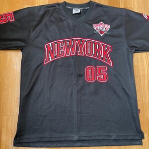 May include: A dark grey mesh jersey with a V-neck, displaying "NEW YORK" in red with a white outline across the chest, and the number "05" below. The sleeves have the number "5" in red. The jersey also has a logo that says "FUBU ATHLETICS 1992".