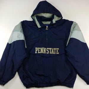 Puede incluir: Chaqueta con capucha azul marino con paneles grises en los hombros y el texto "PENN STATE" en el pecho. La chaqueta tiene cierre de media cremallera y capucha con cordón. Se ve un logotipo de Starter.