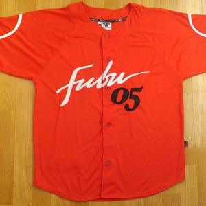 May include: Red baseball jersey with white trim and a white "Fubu 05" logo.