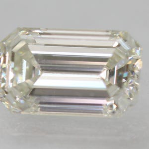 May include: A clear emerald cut diamond with facets that reflect light.