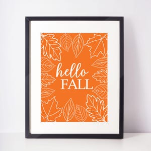 Può includere: Un design di arte da parete stampabile con uno sfondo arancione con contorni bianchi di foglie e il testo "hello fall".
