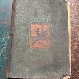 May include: A vintage hardcover book titled Elson Basic Readers Primer with a dark green fabric cover. The front features an orange rectangular illustration of a person riding a horse, surrounded by intricate green scrollwork and decorative patterns.