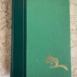 May include: A vintage book with a green cover and a dark green spine. The cover features a gold-colored illustration of a chipmunk. The book's pages are bound together, and the cover has a textured appearance.