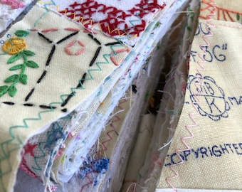May include: A handmade fabric journal with pages of various embroidered and stitched fabrics. The cover features red cross-stitch embroidery, floral designs, and colorful stitching. The edges are secured with zigzag stitching, showcasing a vintage aesthetic.