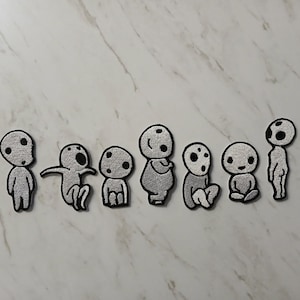 May include: Seven embroidered patches depicting stylized humanoid figures. Each patch has a grey body, a black outline, and a round head with two black spots. The figures are in different poses, including standing, sitting, and kneeling.