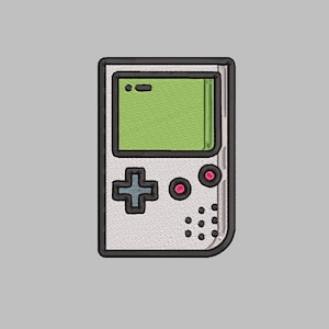 May include: A white handheld video game console with a green screen, a black plus button, and two pink buttons. The console has a black border and a gray background.