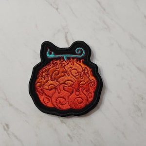 May include: Embroidered patch with a flame-like design in orange and red, outlined in black. A teal swirl and line accent the top. The patch is likely for clothing or accessories, and is suitable for sewing.