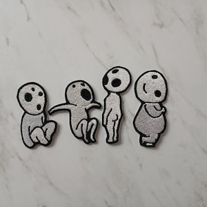 May include: Four embroidered patches depicting a cartoon character in different poses. The characters are light grey with black eyes and a black outline. The patches are on a white marble surface.