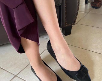 May include: A pair of black leather flats with a pointed toe and a large metal buckle featuring the letter "D".