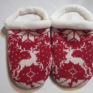 May include: A pair of red and white knitted slippers with a reindeer pattern. The slippers have a white fleece lining.