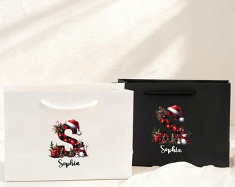 May include: Two gift bags, one white and one black, with white handles. Each bag features a festive design of the letter "S" decorated with Christmas ornaments, a Santa hat, and the name "Sophia".