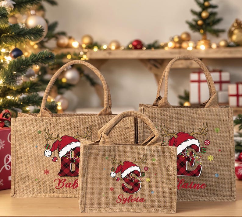 May include: Three burlap tote bags with handles, each featuring a Christmas design. The design includes a Santa hat, antlers, and a letter in a plaid pattern. Names are printed below the letters.