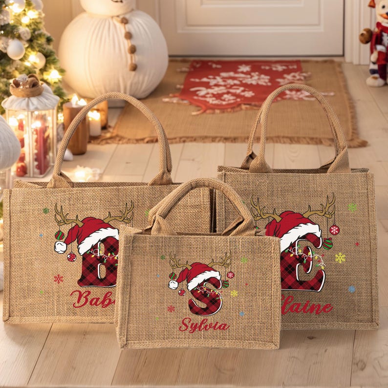 May include: Three burlap tote bags with Christmas-themed designs. Each bag features a red plaid letter wearing a Santa hat and reindeer antlers. The bags are personalized with names in red script, perfect for holiday gifting.