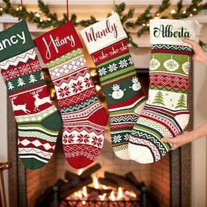 Peut inclure: Quatre chaussettes de Noël en tricot avec des motifs festifs de rennes, de flocons de neige et de bonhommes de neige en rouge, vert et blanc. Chaque chaussette porte un prénom brodé sur le revers : Nancy, Hilary, Mandy et Alberta.