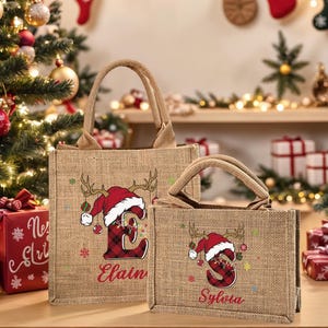 May include: Two burlap tote bags with Christmas-themed designs. Each bag features a reindeer antler and Santa hat design with a letter and name. The larger bag says "Elain" and the smaller bag says "Sylvia".