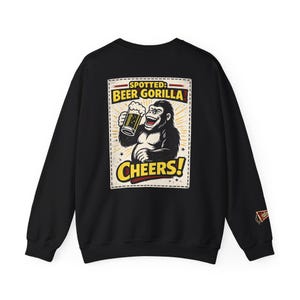 May include: A black long-sleeve sweatshirt featuring a rectangular graphic on the back. The graphic depicts a smiling gorilla holding a beer mug with foam, surrounded by the text SPOTTED: BEER GORILLA! CHEERS! A small pennant logo is on the sleeve.